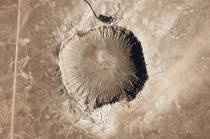 Aerial view of the Meteor Crater and Visitor Center that houses indoor viewing, Interactive Discovery Center, a wide screen movie theater, restaurant, and gift shop, located on the crater rim. Image Credit: NASA Earth Observatory/Public Domain.