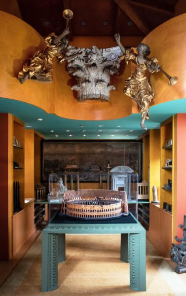 A portion of Piraneseum's collection of 19th century and earlier architectural mementos, including models, pictures and ornament. Front and center is a large, carved cork model of the Roman Colosseum, fashioned in Rome in the 1840s by Luigi Carotti. The model is installed in a Piraneseum-designed vitrine with an Optium Museum Acrylic cover. Above is a carved wood pilaster capital, designed in 1799 by Charles Bulfinch, the first American-born architect. This was originally part of the State House in Boston, before being replaced in the 1960s by a more maintenance-free likeness. The flanking angels, in carved wood and gilded, are south German baroque, fashioned in the later 17th century.