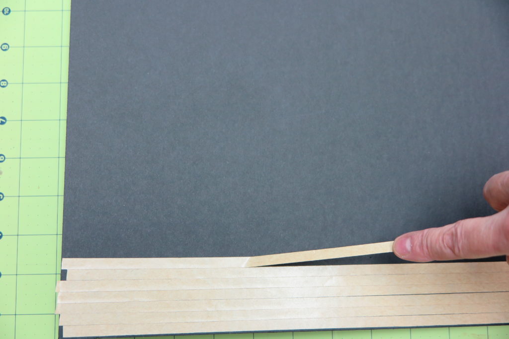 Hand applying adhesive strips to a backing board for artwork mounting.