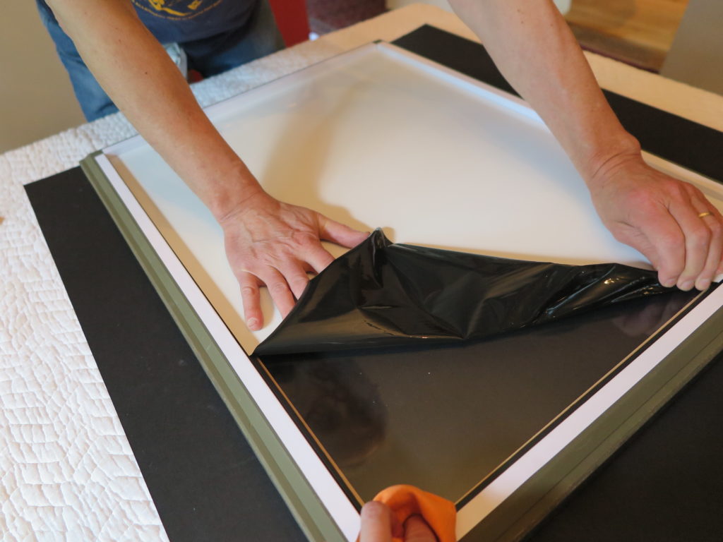 Hands peeling back the protective tape during artwork framing process.