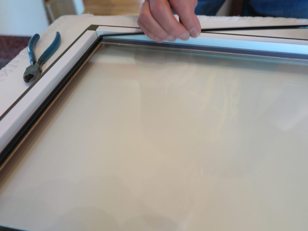 Hand installing a black spacer strip along the edge of glazing inside a frame.
