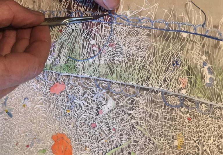 Applying and cutting cotton threads to hang the papercuts from the display rod. Photo by Alisa Vincentelli.