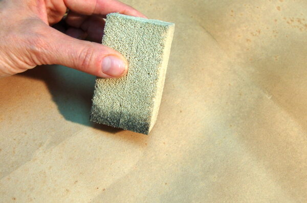 A hand using a "dry cleaning" or chemical sponge on a surface to mechanically lift and absorb soot residue without liquids.