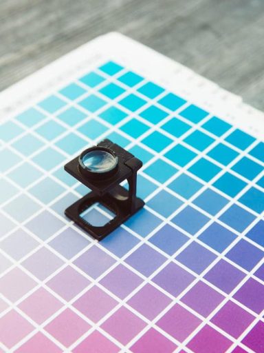 Linen tester magnifying glass placed on a color chart used in graphic design and printing.
