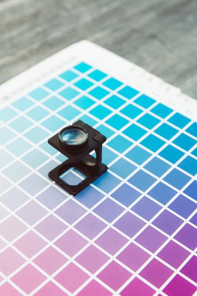 Linen tester magnifying glass placed on a color chart used in graphic design and printing.