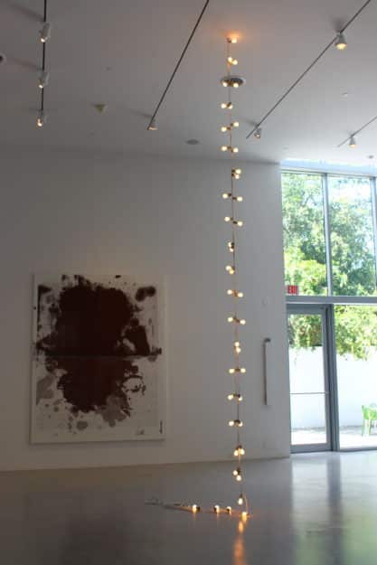 Modern museum gallery featuring a vertical light installation and large abstract artwork near floor-to-ceiling windows.